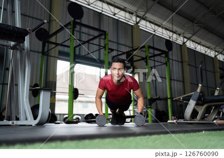 Wellness and Fitness. Man doing push-ups with dumbbells for upper body strength at gym. 126760090