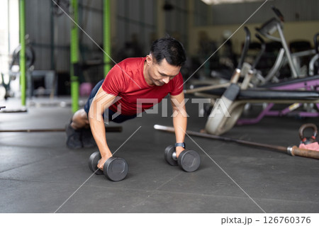 Wellness through Strength Training. Man executing push-up with dumbbells in gym. 126760376