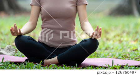 Wellness through Meditation. Close-up of a woman meditating on a yoga mat in a park. 126760497