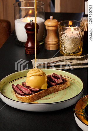 Delicious beef bruschetta with poached egg and cheese sauce being poured on top Delicious beef bruschetta with poached egg and cheese sauce being poured on top 126760762