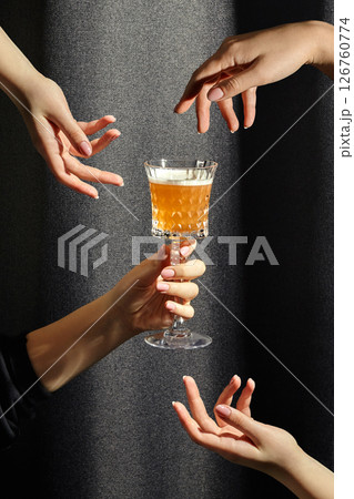Many hands reaching for elegant crystal glass holding refreshing cocktail Many hands reaching for elegant crystal glass holding refreshing cocktail 126760774