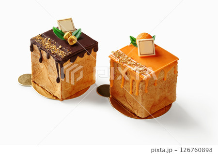 Two small square cakes with chocolate and orange topping resting on golden coasters Two small square cakes with chocolate and orange topping resting on golden coasters 126760898
