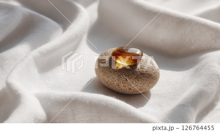Amber Gemstone on Beige Pebble Resting on White Fabric in Soft Light 126764455