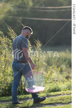 Man carrying a birdcage outdoors on a sunny day. Man carrying a birdcage outdoors on a sunny day. 126764511