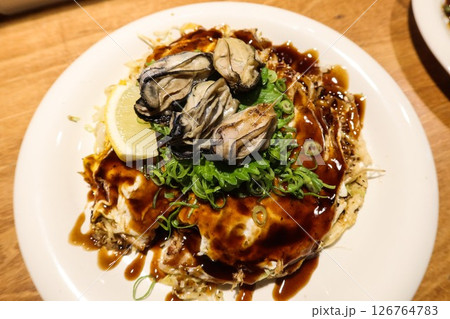close up of Japanese pan fried Hiroshima Okonomiyaki with seafood and seaweed as toppings, udon noodles at the bottom of the omelette. close up of Japanese pan fried Hiroshima Okonomiyaki with seafood and seaweed as toppings, udon noodles at the bottom of the omelette. 126764783