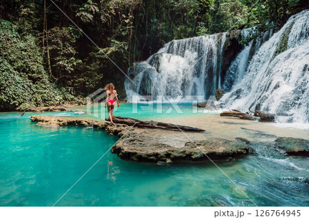 Woman in swimsuit on rock at scenic cascade waterfalls with turquoise water 126764945