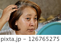 A woman looks at her gray hair in the mirror. 126765275