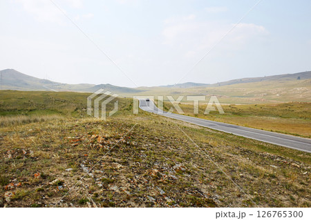 The long highway stretches through vast meadows under a clear sky. 126765300