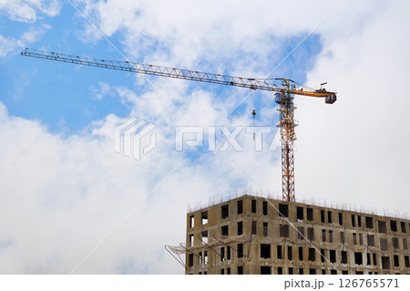 A crane on a construction site against a blue sky with clouds. 126765571