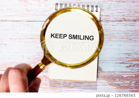 KEEP SMILING words cognized with a magnifying glass in a blank notebook 126766565