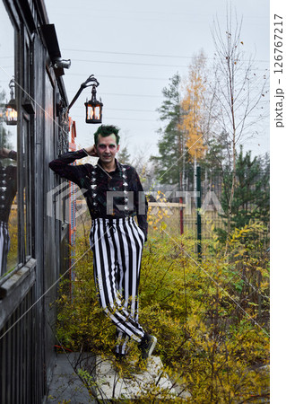 A Quirky Clown Dressed in Striped Pants Poses Cheerfully Against a Colorful Autumn Landscape 126767217