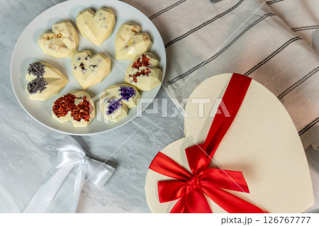 Heart-shaped white chocolates with floral toppings on plate and gift box with red ribbon Heart-shaped white chocolates with floral toppings on plate and gift box with red ribbon 126767777