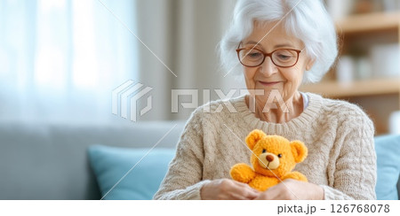 Elderly Lady Enjoys Playful Moment with Orange Felt Bear 126768078