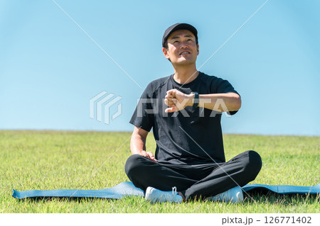 スマートウォッチ,スマートバンドを使ってヨガ,ストレッチ,ヘルスケアをするスポーツウェア姿の中年男性 126771402