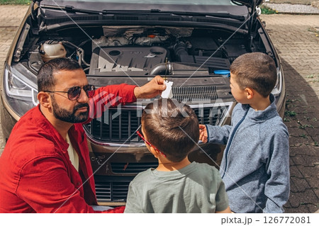 Father and sons repairing car together with the hood open. A heartfelt moment of bonding, fatherhood, parenting, teamwork, and learning. Celebrating Father Day through shared hands-on experience. 126772081