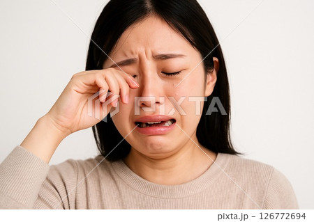 白背景で涙を拭う女性クローズアップ横長写真 126772694
