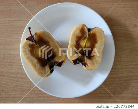 spoiled bad apple cut in half revealing brown discoloration on plain white plate. closeup. 126772844
