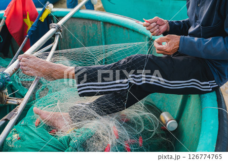 Vietnamese male fisherman repairs a fishing net on traditional basket boat on beach by the sea in a fishing village in Vietnam 126774765