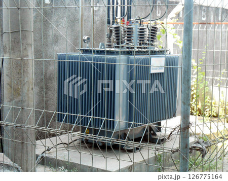 High Voltage Transformer Enclosed Behind Metal Fencing in an Industrial Setting High Voltage Transformer Enclosed Behind Metal Fencing in an Industrial Setting 126775164