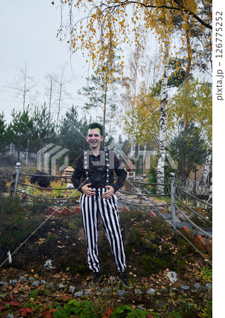 A Mysterious Clown in Colorful Striped Pants Stands Amid Beautiful Autumn Scenery 126775252