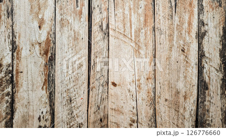 Weathered wooden planks with rustic aged texture in natural brown and beige tones forming a vertical wooden surface with visible grain knots cracks and rough imperfections in an old outdoor setting 126776660