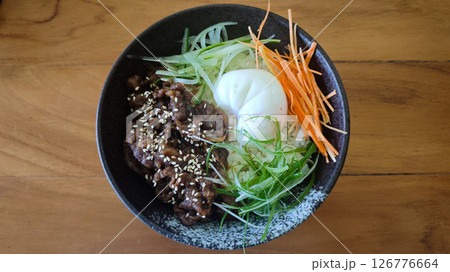 Black ceramic bowl of caramelized beef sesame soft-boiled egg and fresh julienned vegetables over rice on a rustic wooden table Black ceramic bowl of caramelized beef sesame soft-boiled egg and fresh julienned vegetables over rice on a rustic wooden table 126776664