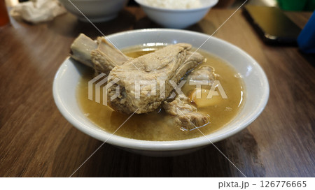 Steaming Bowl of Pork Rib Soup with Garlic and Light Broth Served in a White Ceramic Bowl on a Wooden Table in a Casual Dining Setting with a Blurred Background Steaming Bowl of Pork Rib Soup with Garlic and Light Broth Served in a White Ceramic Bowl on a Wooden Table in a Casual Dining Setting with a Blurred Background 126776665
