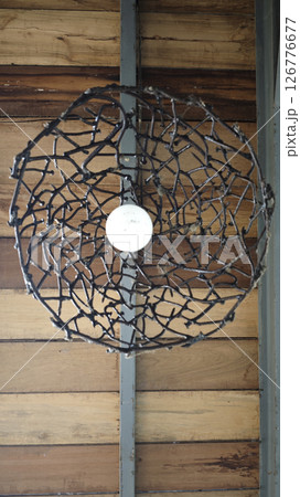 Handmade industrial pendant light with welded metal rods and an exposed bulb, hanging against a rustic wooden and metal background. Handmade industrial pendant light with welded metal rods and an exposed bulb, hanging against a rustic wooden and metal background. 126776677