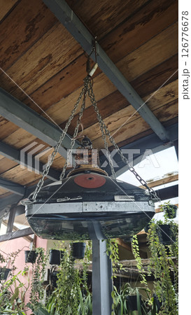 Hanging industrial lamp made from recycled TV parts and metal chains under a rustic wooden ceiling with green plants in the background. 126776678