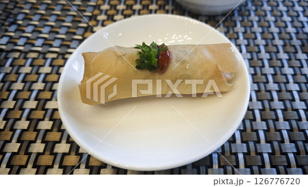 Crispy Spring Roll Garnished with Parsley and Chili Sauce on White Plate with Woven Table Mat Background 126776720