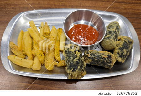 Plate of crispy Korean fried seaweed rolls and seasoned French fries served with spicy red dipping sauce on a silver tray placed on a wooden table Plate of crispy Korean fried seaweed rolls and seasoned French fries served with spicy red dipping sauce on a silver tray placed on a wooden table 126776852