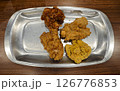 Close-up of assorted fried chicken with four flavors served on a shiny silver plate on a wooden table in a casual dining setting 126776853