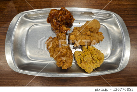 Close-up of assorted fried chicken with four flavors served on a shiny silver plate on a wooden table in a casual dining setting Close-up of assorted fried chicken with four flavors served on a shiny silver plate on a wooden table in a casual dining setting 126776853