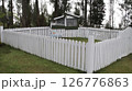White wooden fence surrounding an outdoor rabbit shelter with greenery and tall trees in a peaceful countryside garden setting 126776863