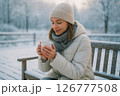 雪景色の中、ホットドリンクを手にほっと一息つく女性（癒しと温もり） 126777508