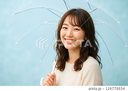 淡い水色の背景で傘を持ち微笑む茶髪の若い日本人女性 126778834