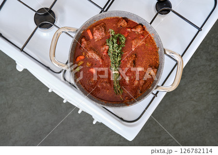 Delicious beef stew simmering on the stovetop with fresh herbs and vegetables added for flavor 126782114