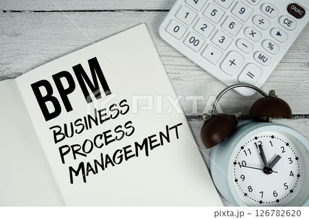 BPM Business Process Management text on paper notebook page with alarm clock and calculator on wooden background 126782620