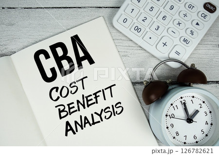 CBA Cost Benefit Analysis text on paper notebook page with alarm clock and calculator on wooden background 126782621