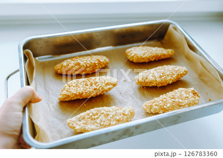 Raw frozen breaded chicken pieces on a baking sheet. Raw frozen breaded chicken pieces on a baking sheet. 126783360
