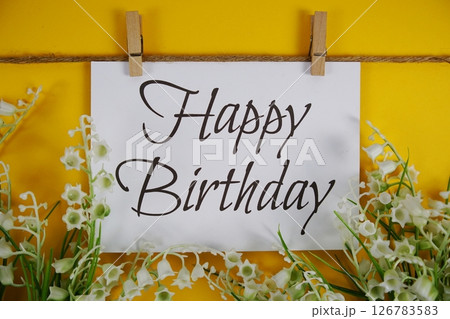Happy Birthday text on paper card with flower blooming decoration on yellow background Happy Birthday text on paper card with flower blooming decoration on yellow background 126783583