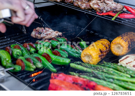 Grilling chicken, corn cobs, paprika and asparagus with temperature control,. Meat tongs in human hands 126783651