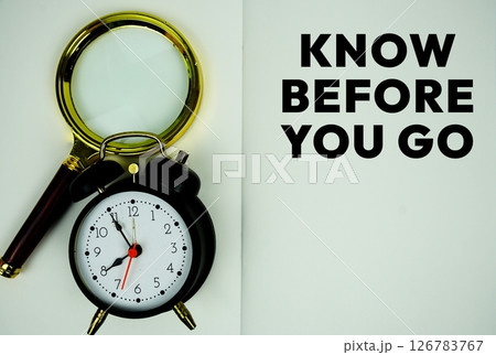 Know Before You Go text with magnifying glass and alarm clock flat lay on notepad background 126783767