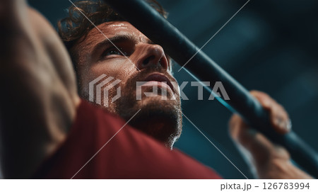 Focused man engages in intense pull-ups at a bustling gym 126783994