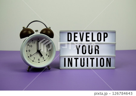 Develop Your Intuition text on LED lightbox with alarm clock on purple background 126784643