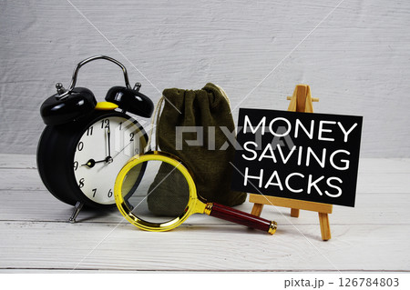 Money Saving Hacks text with alarm clock and magnifying glass on wooden background 126784803