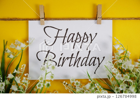 Happy Birthday text on paper card with flower blooming decoration on yellow background Happy Birthday text on paper card with flower blooming decoration on yellow background 126784998