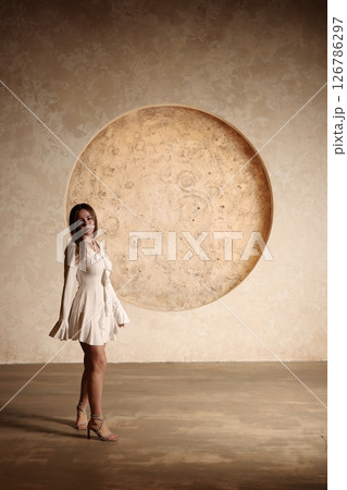 An Elegant Woman Wearing a Beautiful White Dress Stands Against a Large Circle Background An Elegant Woman Wearing a Beautiful White Dress Stands Against a Large Circle Background 126786297