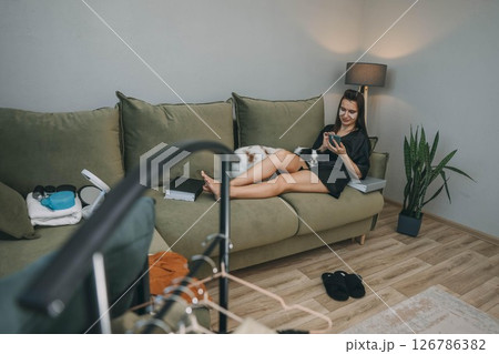 woman relaxing with smartphone during morning beauty routine with japanese chin dogs at home, clothes rack 126786382