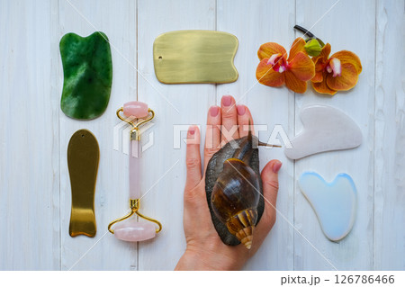 Spa concept gua sha massage body and face care and snails achatina on hand, flat lay. High quality photo Spa concept gua sha massage body and face care and snails achatina on hand, flat lay. High quality photo 126786466